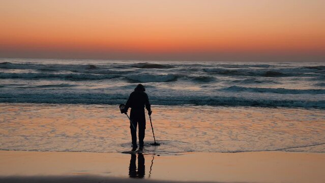 In the early morning sunrise a treasure hunter sweeps his metal detector over the beach sand in Durban, South Africa.