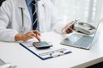 Healthcare costs and fees concept.Hand of smart doctor used a calculator and smartphone, tablet for medical costs at hospital in morning light.