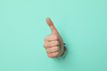 Female hand showing thumb up on turquoise background
