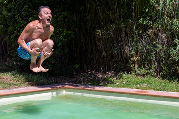 Middle-aged white man dives into the pool cannonball style, with a comical expression