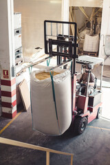 Worker transporting a large sack full of food with a forklift inside a warehouse