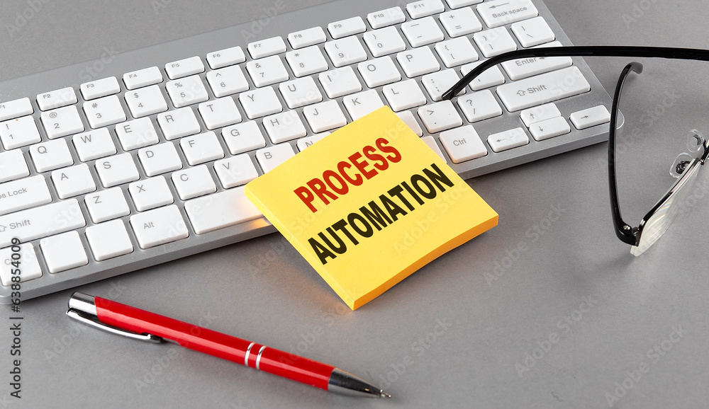 Aufkleber process automation text on a sticky with keyboard, pen glasses on grey background