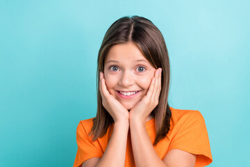 Fototapeta premium Portrait of good mood nice schoolgirl dressed orange t-shirt hold palms on cheekbones smiling isolated on turquoise color background