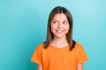 Fototapeta premium Portrait of charming cute little girl looking empty space dreaming wearing orange t-shirt isolated cyan color background