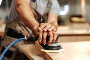 Close up of carpenter hands sanding wood with orbital sander at workshop