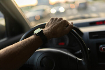 Naklejka premium driving a car, the driver's hands on the steering wheel on a sunny day with a smart watch.