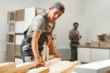 Young carpenter man looking and choosing wood plank at workshop in carpenter wood factory