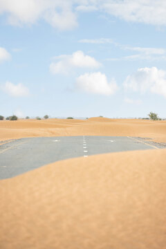 (Selective focus) Stunning view of a deserted road covered by sand dunes. Empty road that run through the Dubai desert. Dubai, United Arab Emirates, (UEA)