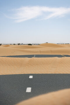 (Selective focus) Stunning view of a deserted road covered by sand dunes. Empty road that run through the Dubai desert. Dubai, United Arab Emirates, (UEA)