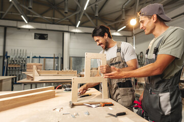 Two young men carpenters making furniture in warehouse of wood factory