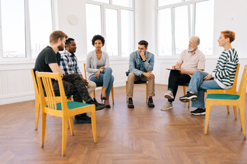Remote view of diverse support group during meeting with professional senior male therapist. Multi-ethnic men and women looking serious during team counselling session. Concept of mental health - obrazy, fototapety, plakaty