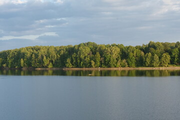 Calm river glade. Sunlit trees can be seen in the distance.