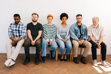 Front view group of tired diverse multiethnic different ages candidates for vacancy sitting on chairs in queue feeling nervous bored waits job interview turn, on white isolated background. HR concept