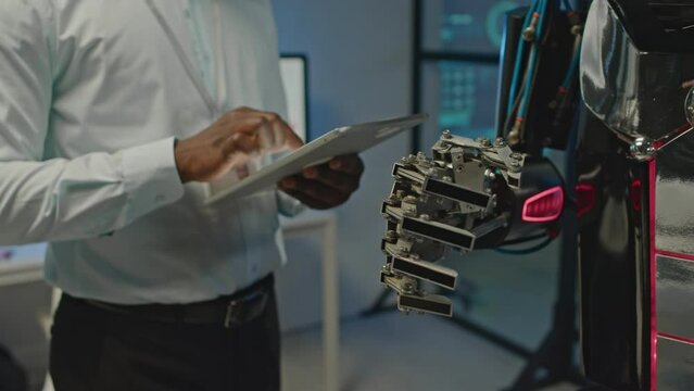 Cropped shot of unrecognizable tech developer operating human robot via digital tablet in scientific labCropped shot of unrecognizable tech developer operating human robot via digital tablet in scient