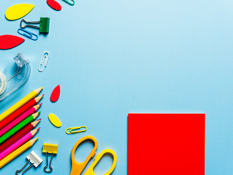 Ein roter Notizzettel, eine Schere und Schulsachen auf einem blauen Hintergrund. Flat lay.