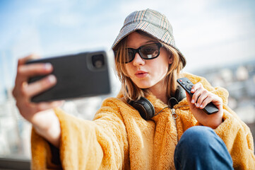 Young pretty woman social media influencer in a yellow fur coat is filming live with her smartphone...