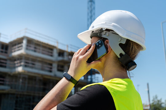 Female engineer at construction site of a building. Woman supervisor talking on the phone. Professional architect businesswoman wearing hard hat safety helmet and reflective clothing vest. - Powered by Adobe