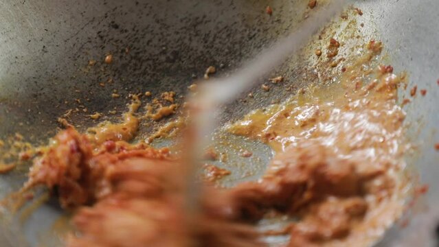 The cook's hands are stir-frying curry paste with oil.
