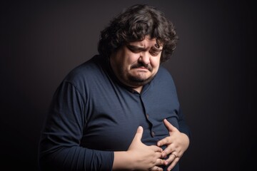 studio shot of a man rubbing his stomach in an expression of discomfort