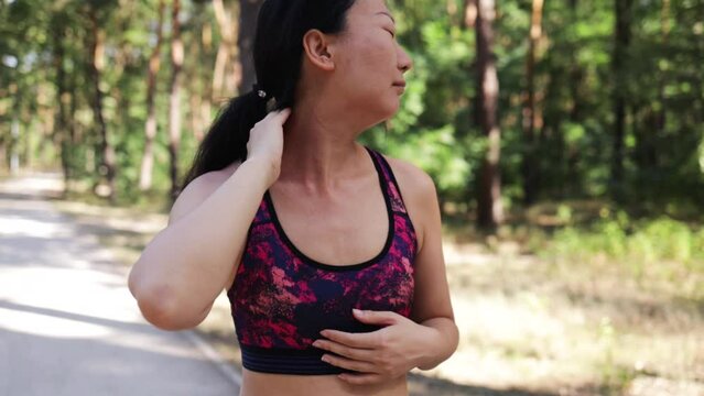 Young asian fitness woman holding her sports injury neck, muscle painful during training