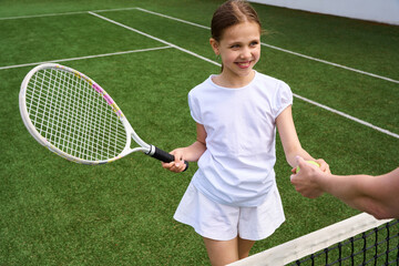 Young tennis player takes ball from hands of young woman