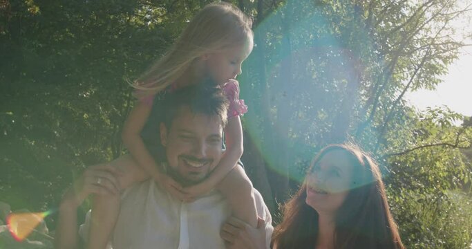 a little girl next to her pregnant mom and dad are walking in the park near the pond