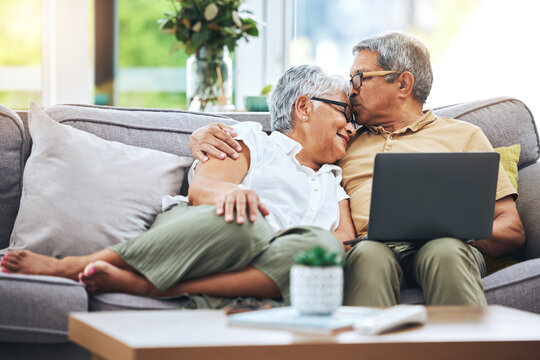 Laptop, love and senior couple on sofa for watching movies, entertainment or streaming in living room. Retirement, marriage and happy man and woman kiss on computer for bonding, relax or film at home