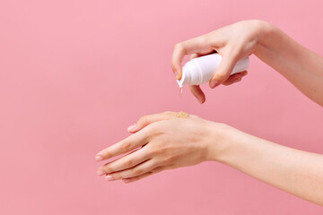 Woman's hand squeezing cream, gel for hands from unmarked bottle with dispenser. Close-up, pastel pink background. Concept of body care.