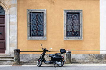 Black scooter parked on sidewalk in front of a historical Italian house with yellow plastered walls, stone pillars and large wooden door