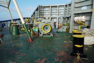 Forward mooring station behind windbreaker with winch and anchor windlass with chain and heaved up white manila rope on working drum of cargo container vessel during passing Atlantic Ocean.