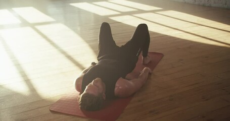 Top view of a man who pumps his pelvic muscles during fitness. Going in for sports a man in a black sports summer uniform lies on a carpet
