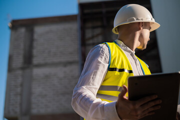 Obraz premium Civil engineer using a tablet, planning a project, builds a modern structure, reading a plan. Architect or engineer working on a construction site.