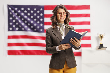 Young academic woman holding book in front of USA flag