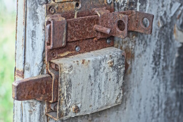 part of an old door with a brown rusty iron latch and a gray overhead metal lock