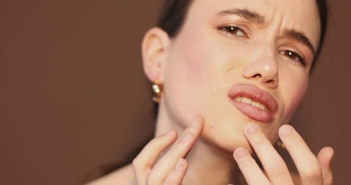 Unhappy girl standing looking in the mirror, checking dry irritated skin. Morning skincare routine. Beautiful girl with not smooth skin crushes red acne on her face. Woman checking skin problem.