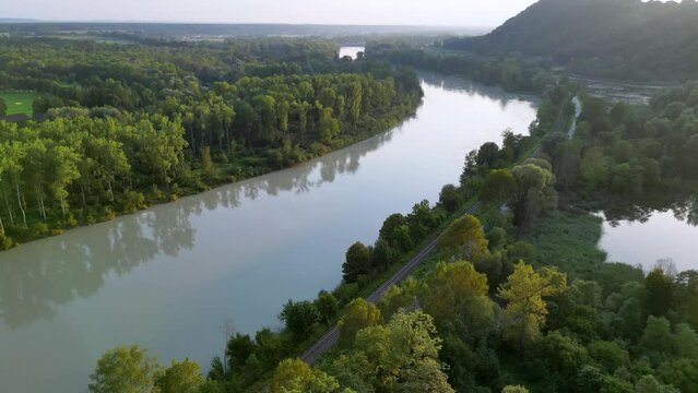 Drone rising next to river Inn, rails and street and lakes with a hill to the rigth in the bavarian sunset