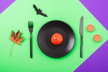 Halloween green and purple table place setting with decorative pumpkin, bat, autumn leaf and orange candles. Top view, flat lay
