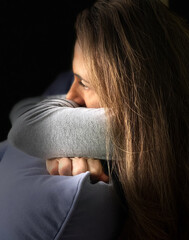 Lonely woman in despair helpless seating in the dark looking sad depressed and lost in thoughts.