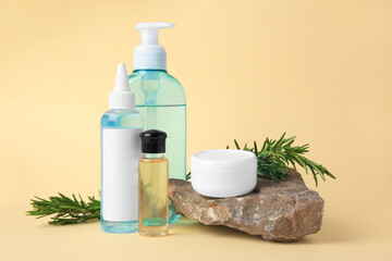 Fototapeta na wymiar Bottles with cosmetic products, stone and rosemary on beige background