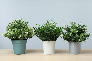 Many different artificial plants in flower pots on wooden table against light grey background