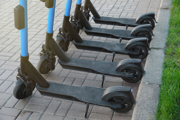 Many modern electric scooters parked on pavement. Rental service