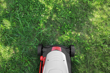 Cutting green grass with lawn mower in garden, top view. Space for text