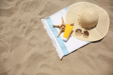 Tube of sunscreen, starfish and beach accessories on sand, top view with space for text. Sun protection care