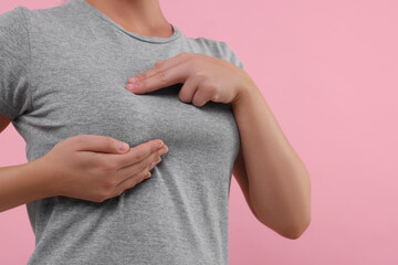 Woman doing breast self-examination on pink background, closeup