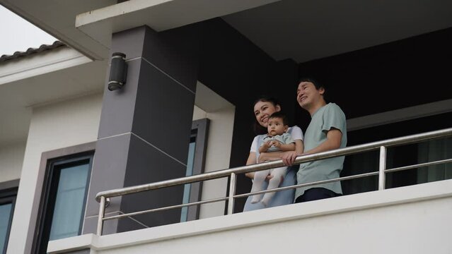 happy family (father, mother and infant baby) talking and looking view at balcony of their house