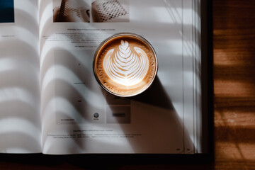A book and coffee latte art in a beautiful sunlight coming through blinds