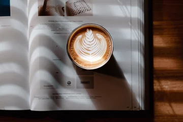 Fotobehang Koffiebar A book and coffee latte art in a beautiful sunlight coming through blinds