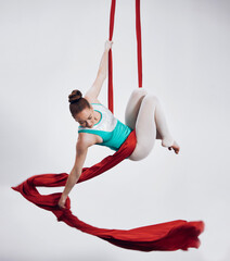 Obraz premium Gymnastics, aerial acrobat and sports with a woman in air for performance and balance. Young athlete person or gymnast hanging on red silk fabric and white background with space, art and creativity
