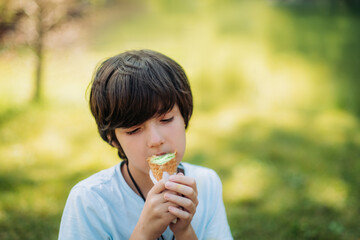 Outdoor portrait of young boy eating ice cream in crispy cone.