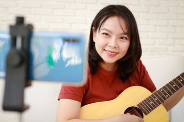 Asian female musician playing guitar online on smartphone. Online music teacher. international music concept